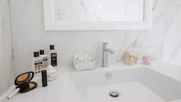 Un baño con lavamanos de mármol, un espejo y distintos artículos de aseo.