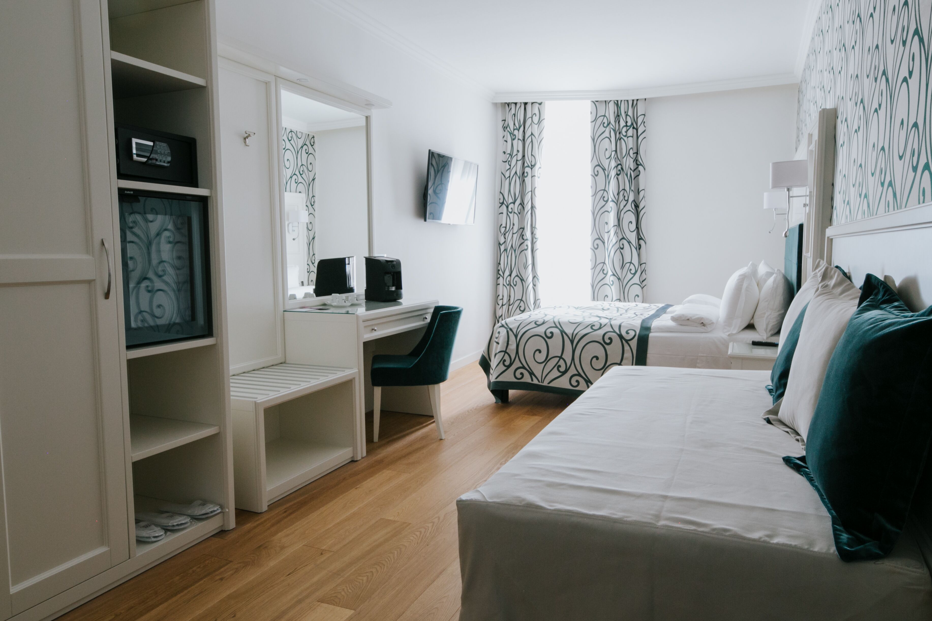 A hotel room with a bed, a desk with a chair, a wardrobe, and a large mirror.