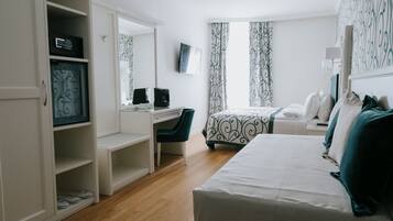 A hotel room with a bed, a desk with a chair, a wardrobe, and a large mirror.