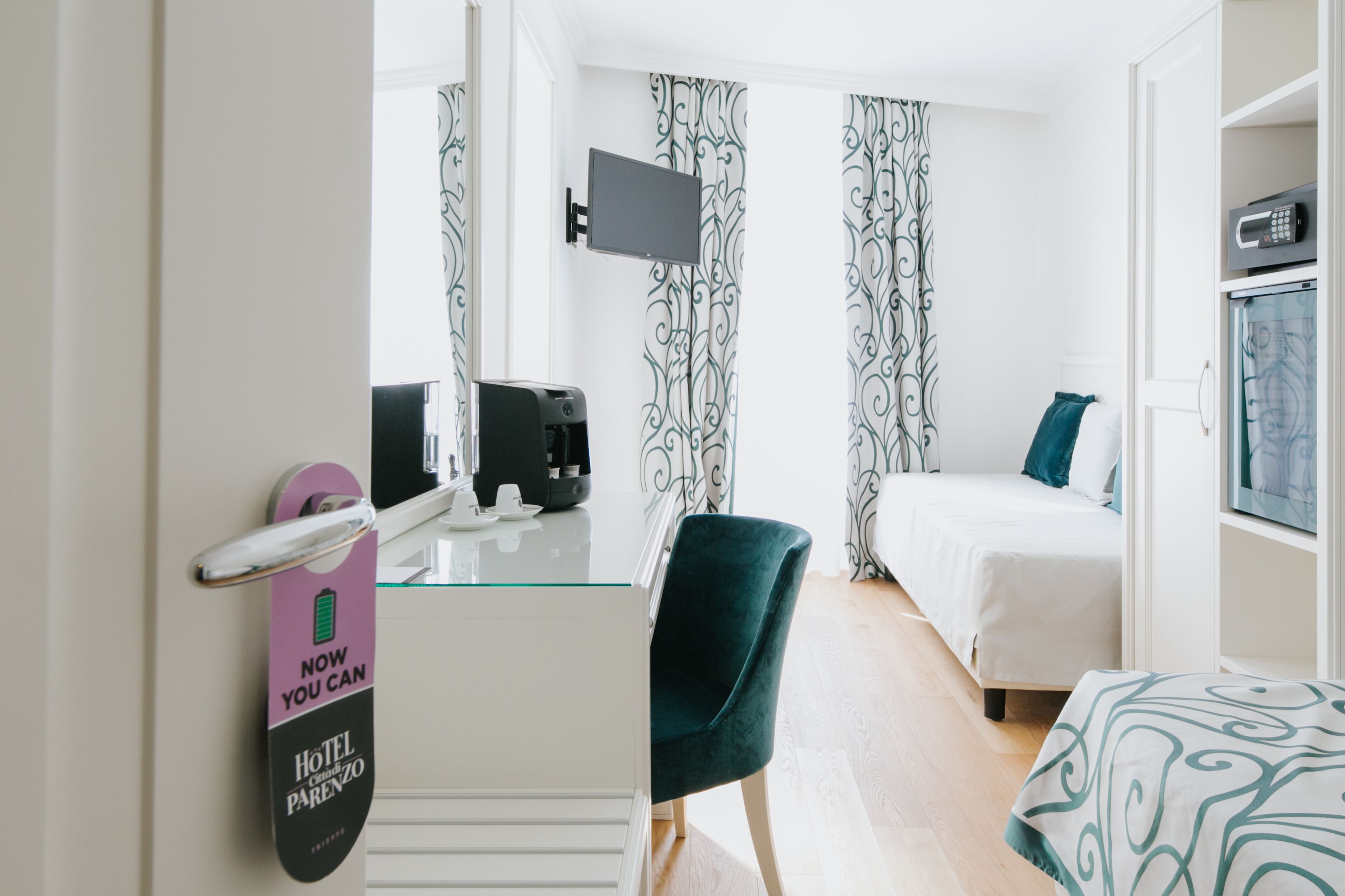 Quarto de hotel com cama, escrivaninha, máquina de café, televisão e minibar.