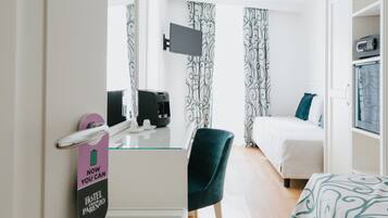 Quarto de hotel com cama, escrivaninha, máquina de café, televisão e minibar.