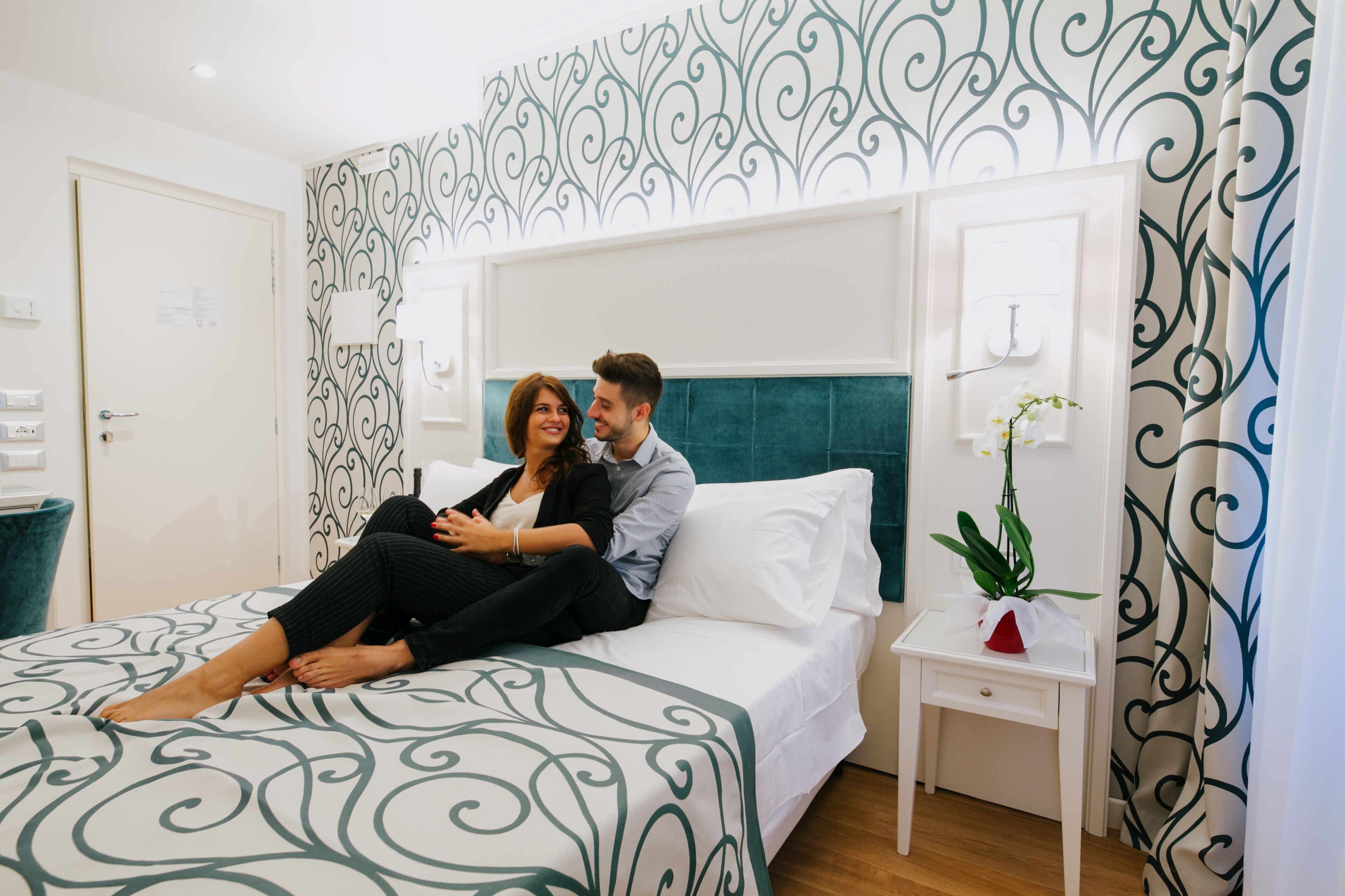 A bedroom with a bed, a nightstand, a potted plant, and a wall with a decorative pattern.