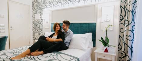 A bedroom with a bed, a nightstand, a potted plant, and a wall with a decorative pattern.