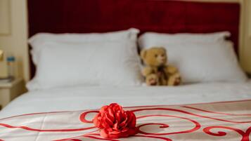 A bed with white linens and a red rose decoration.