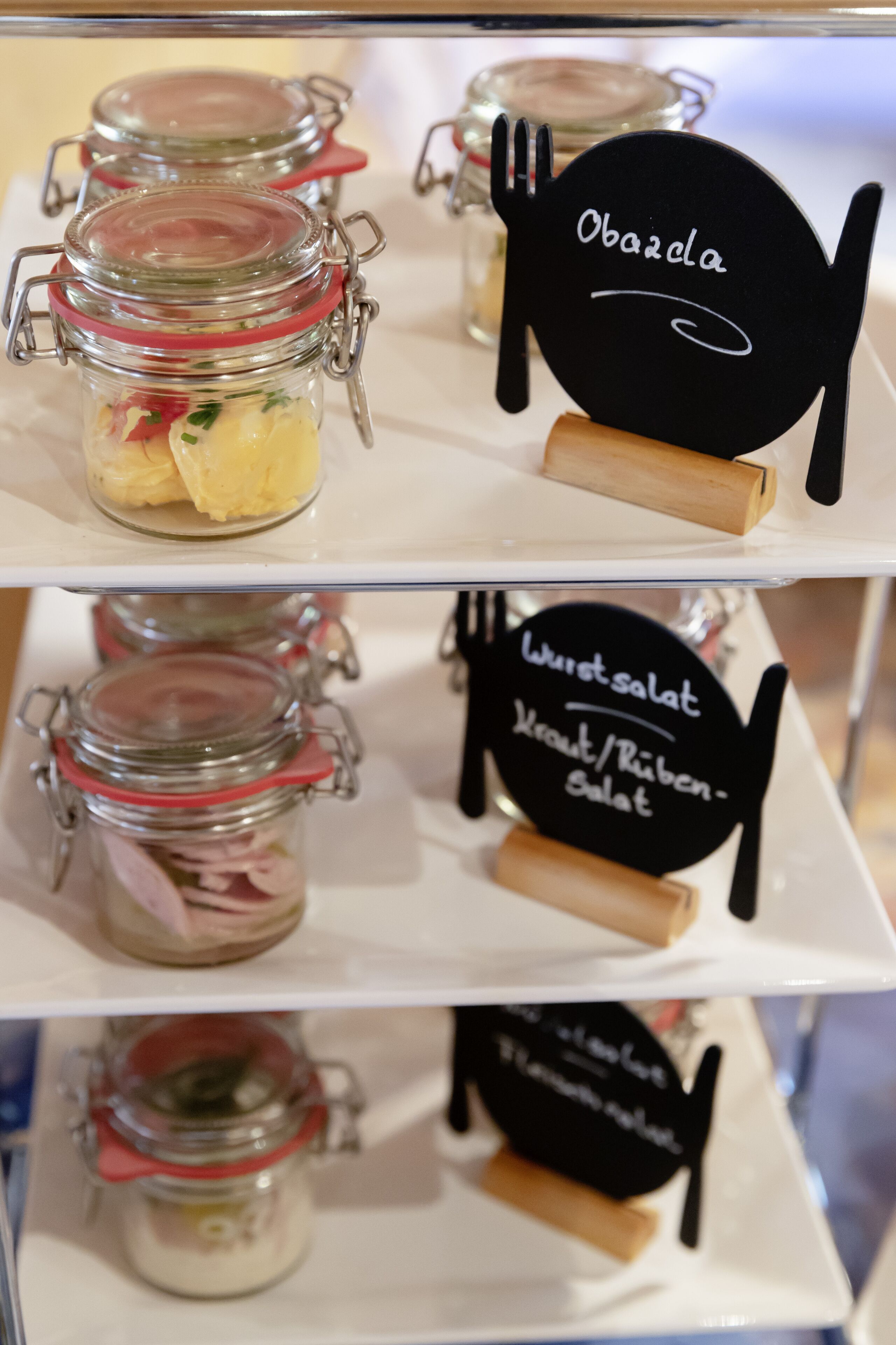 A food display with jars of pickled vegetables and a sign indicating 'Obazela' and 'Wurstsalat'.