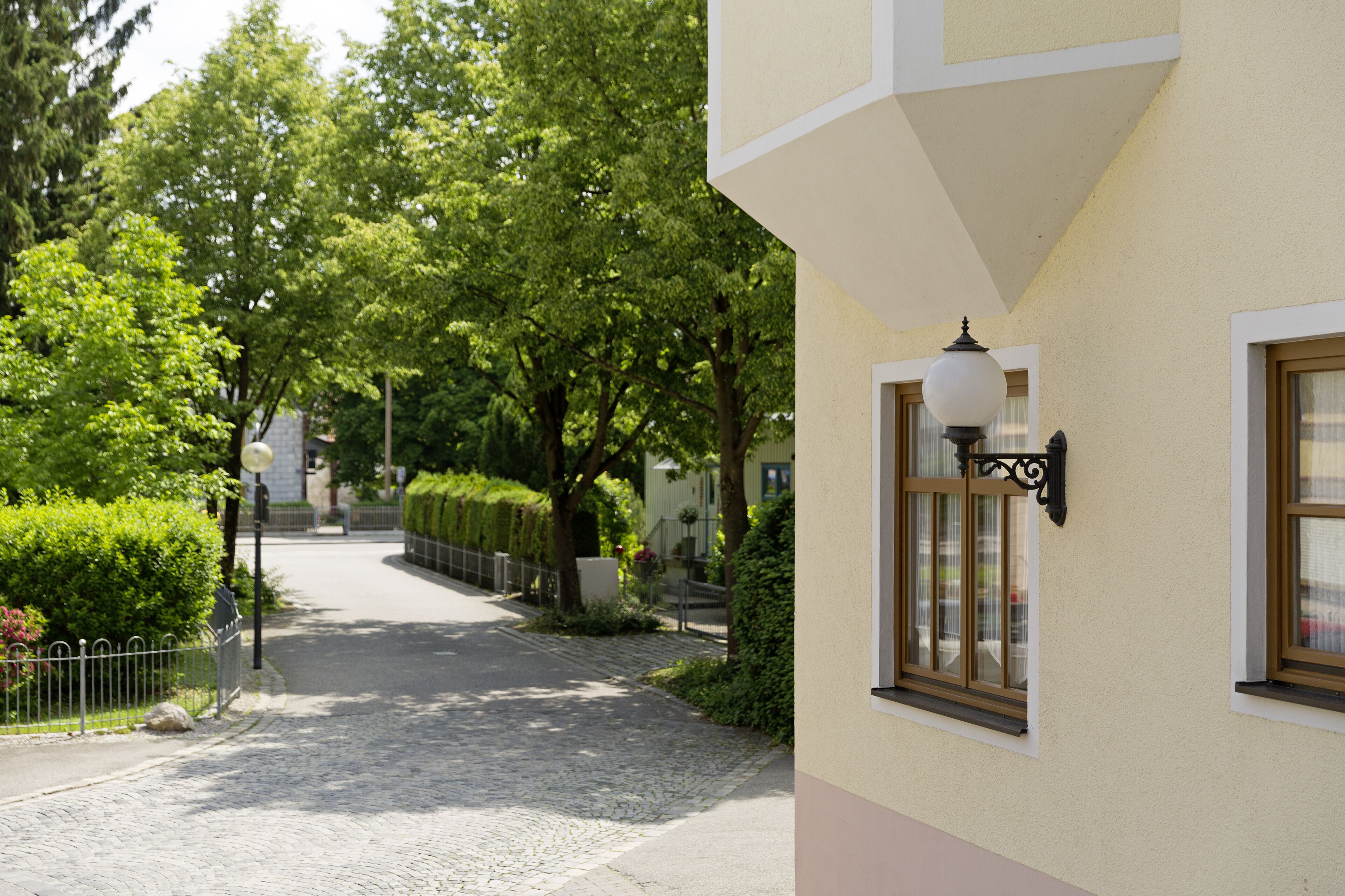Eine von Bäumen gesäumte Kopfsteinpflasterstraße mit einem Gebäude, einer Lampe und einem Fenster.