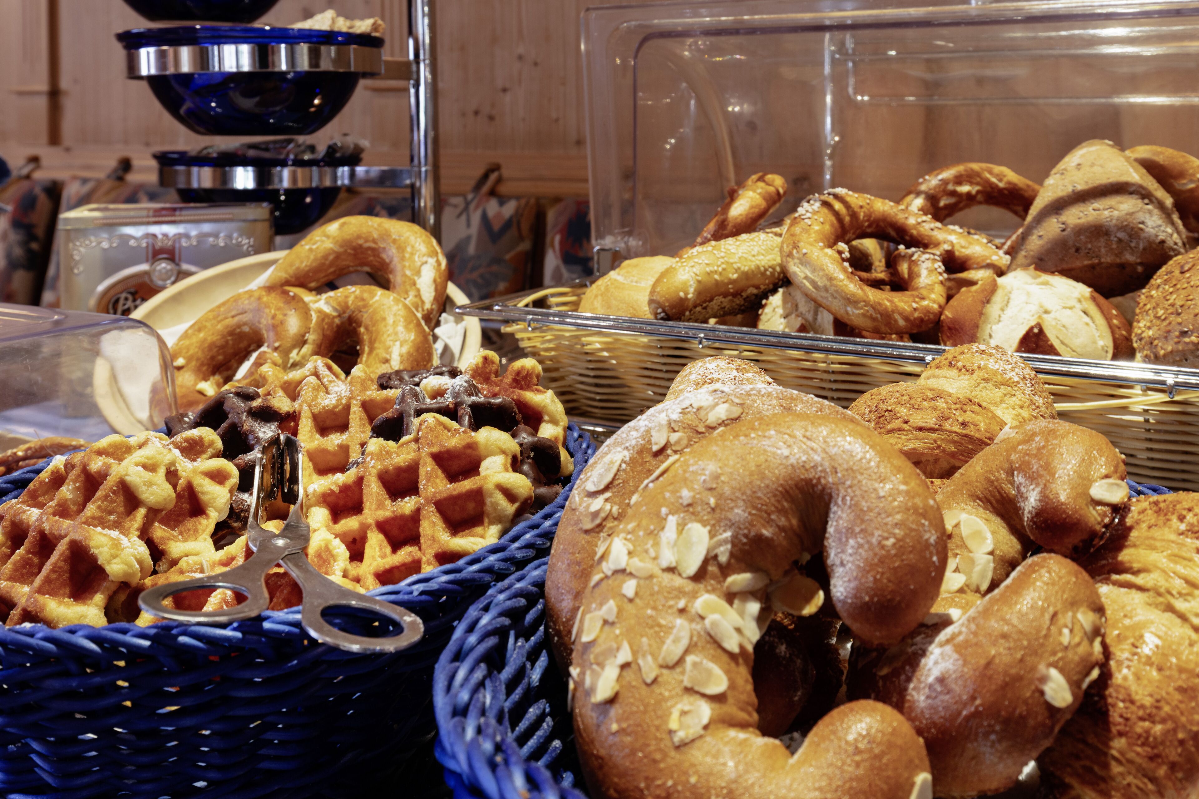 Una exhibición de diversos productos horneados, como gofres, bagels y pasteles, en cestas.