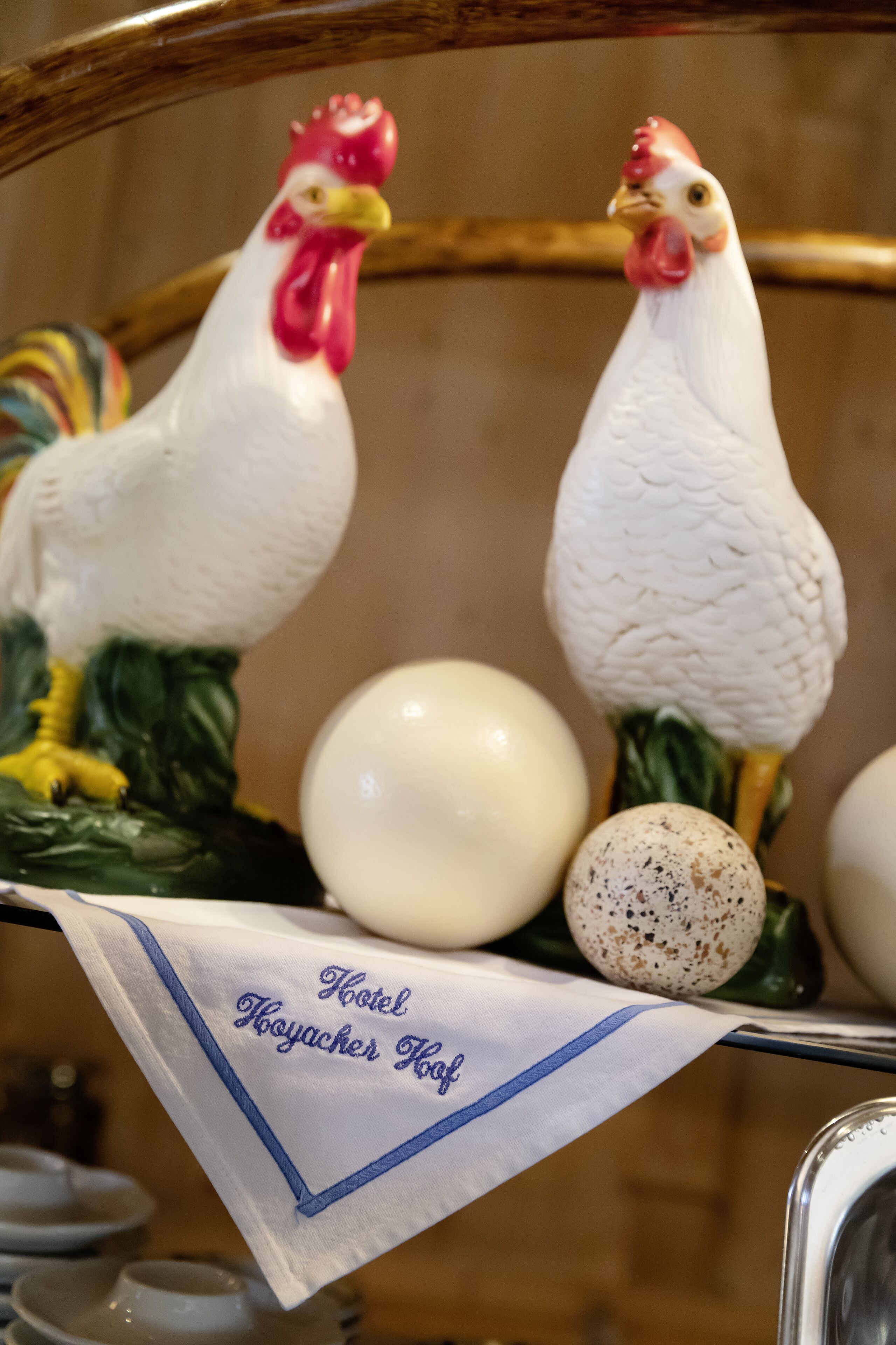 A decorative rooster and hen figurine on a table with a white cloth that reads "Hotel Hojacher Hof."