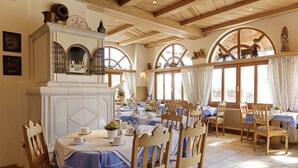 A dining area with tables set for service, a fireplace, and large windows with curtains. - Hotel Hoyacker Hof (Garching)