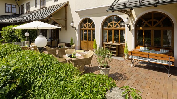 An outdoor patio with wicker furniture, a table, and a bench. - Hotel Hoyacker Hof (Garching)