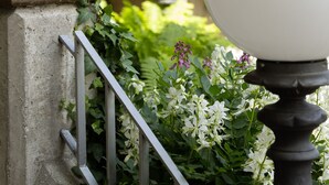A wooden column, a white lamp post, and a garden with flowers and greenery. - Hotel Hoyacker Hof (Garching)