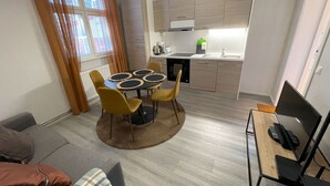 Un espacio habitable compacto con comedor, kitchenette y un pequeño televisor sobre un mueble.