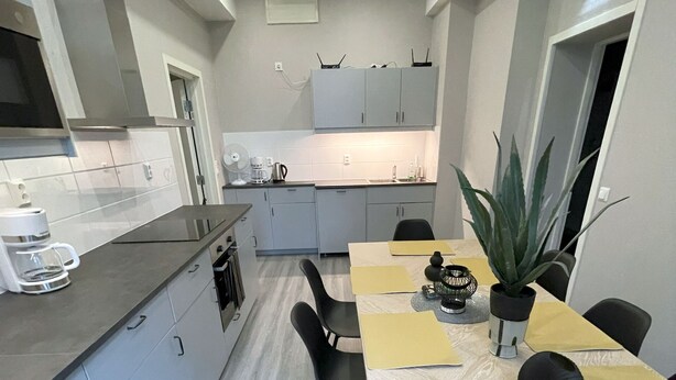 Una cocina compacta con armarios grises, una mesa de comedor con individuales amarillos y una planta en maceta.