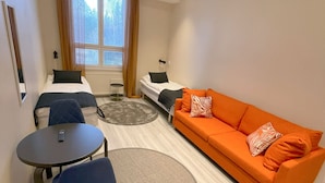 Habitación de hotel compacta con dos camas individuales, un sofá naranja, una mesita redonda y una silla.