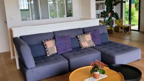 Uma sala de estar moderna com um sofá seccional, uma mesa de centro de madeira e uma janela grande com vista para o verde.