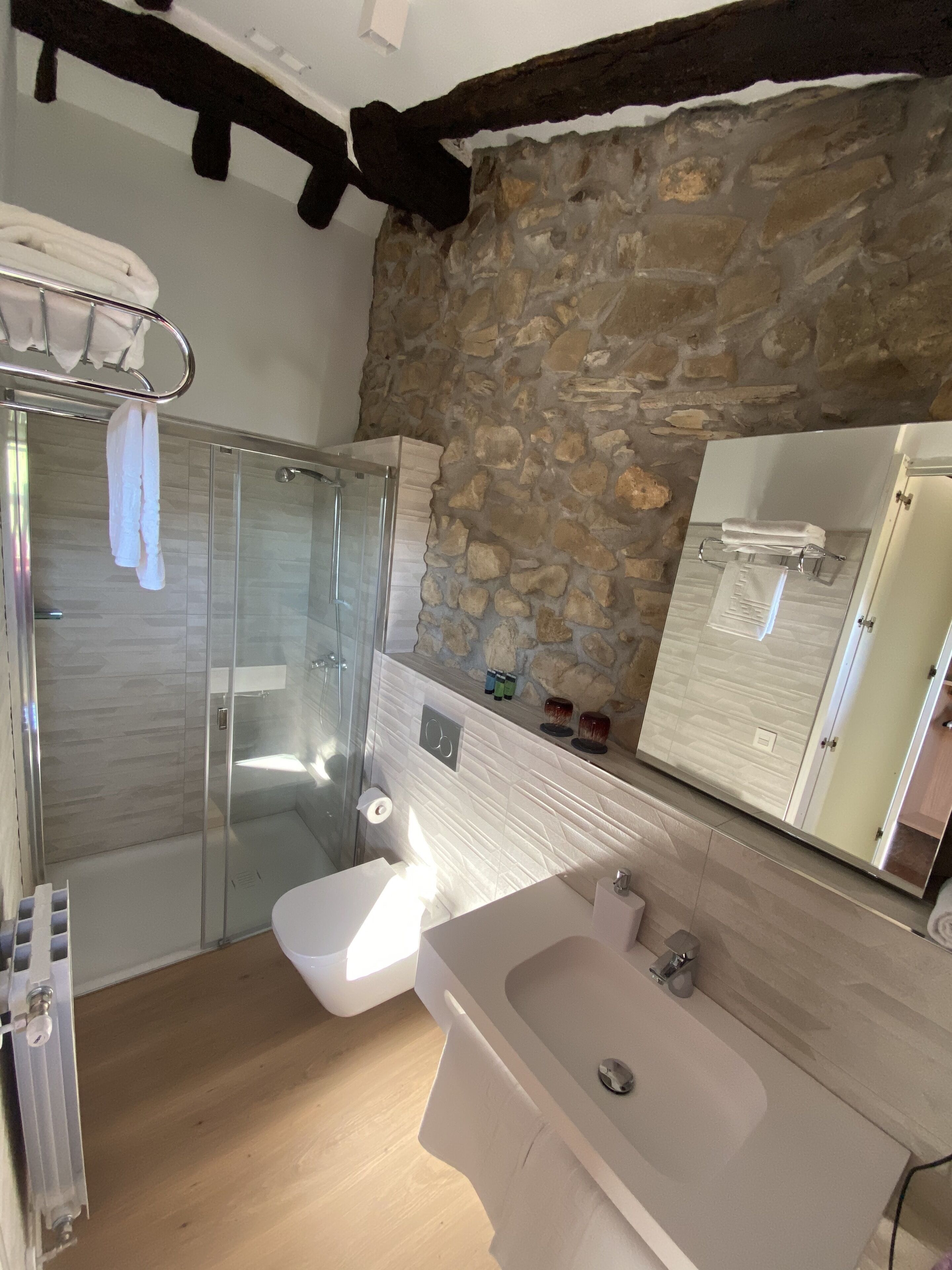 A modern bathroom with a glass shower, a white sink, and a stone accent wall.
