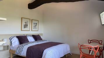 A bedroom with a bed, two framed pictures on the wall, a wooden headboard, and a table with chairs.
