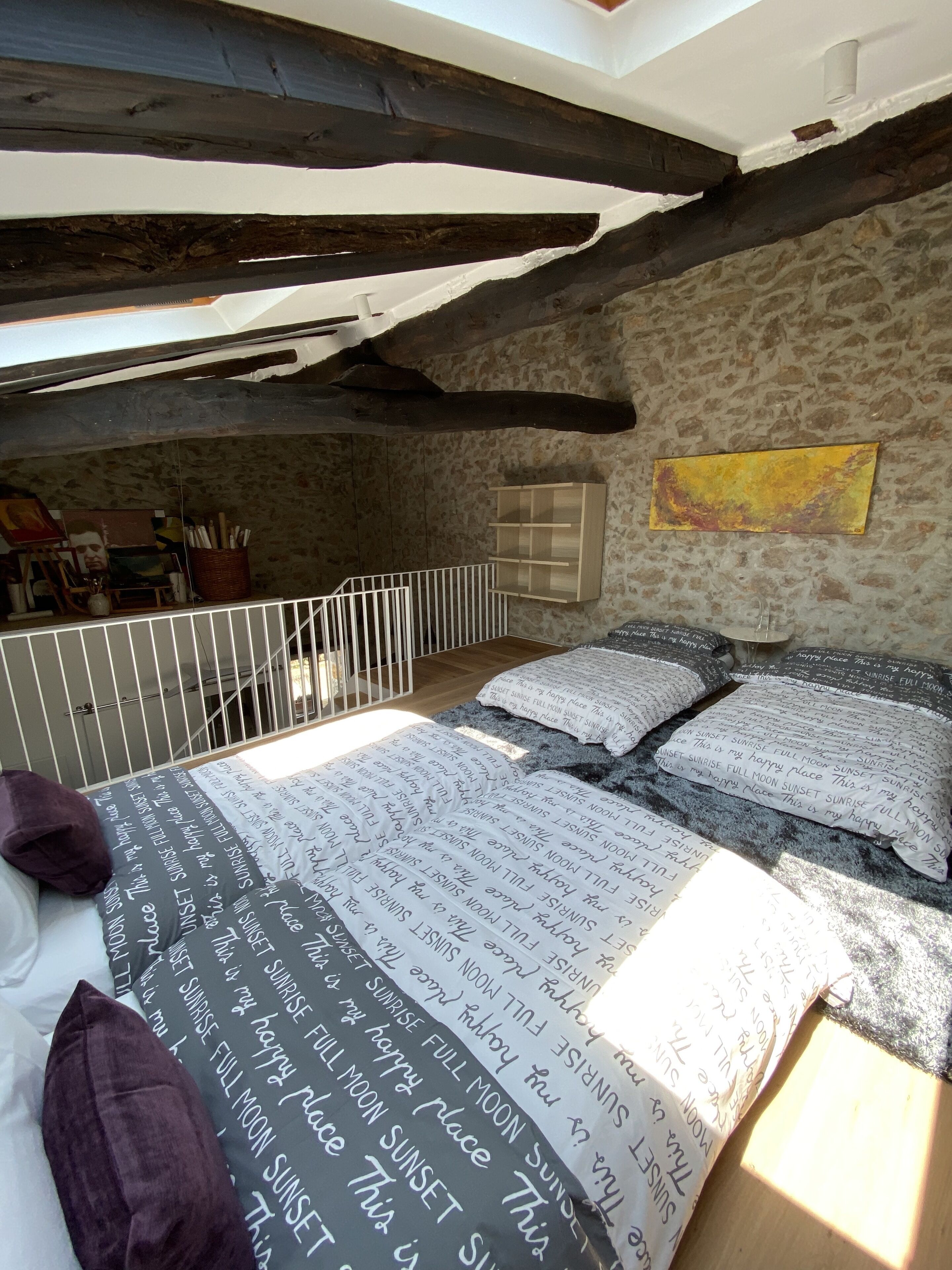 A bedroom with a sloped ceiling, a stone wall, and a bed with patterned bedding.