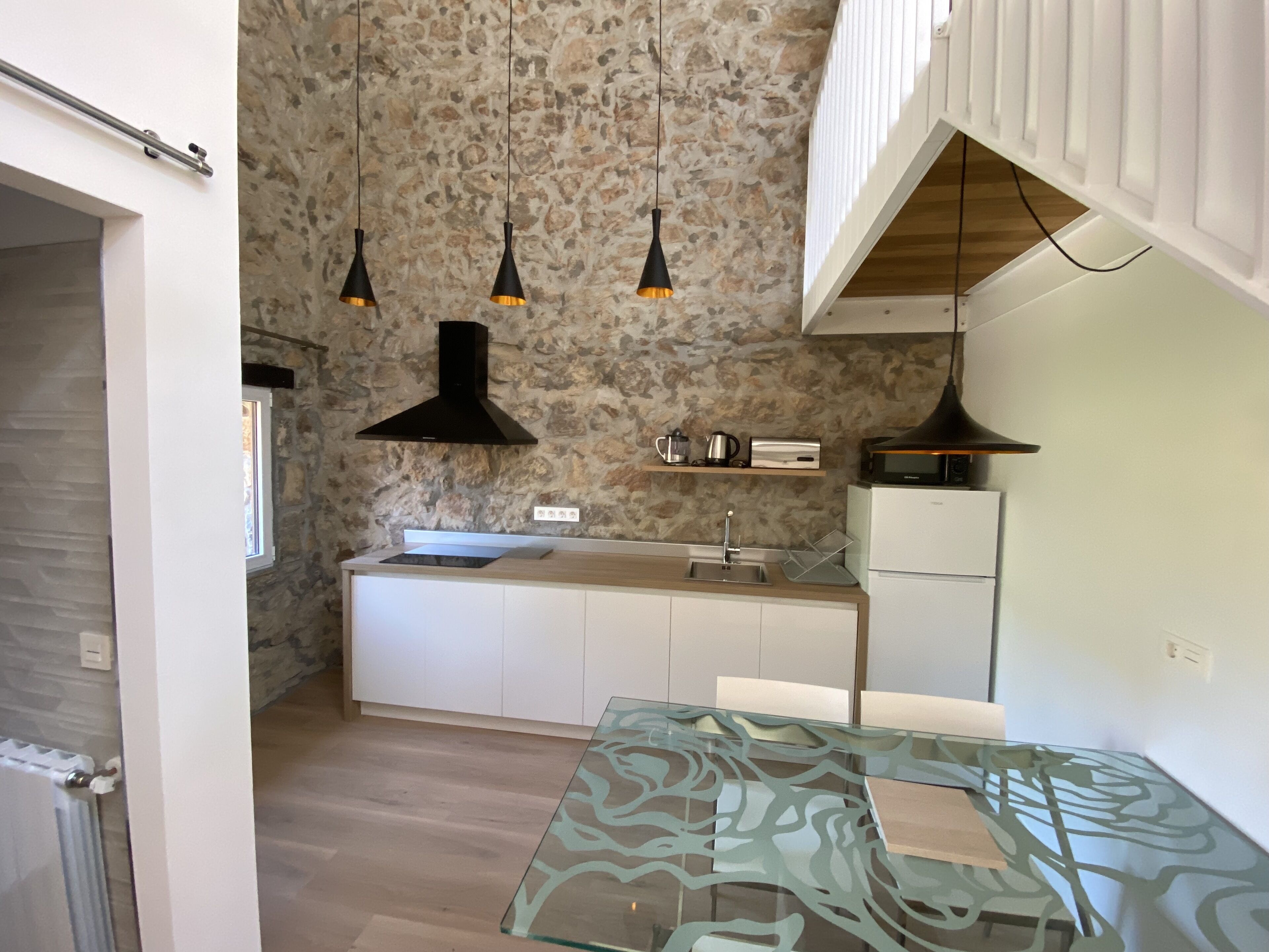 A modern kitchen with a stone backsplash, pendant lights, a microwave, and a glass-top table.