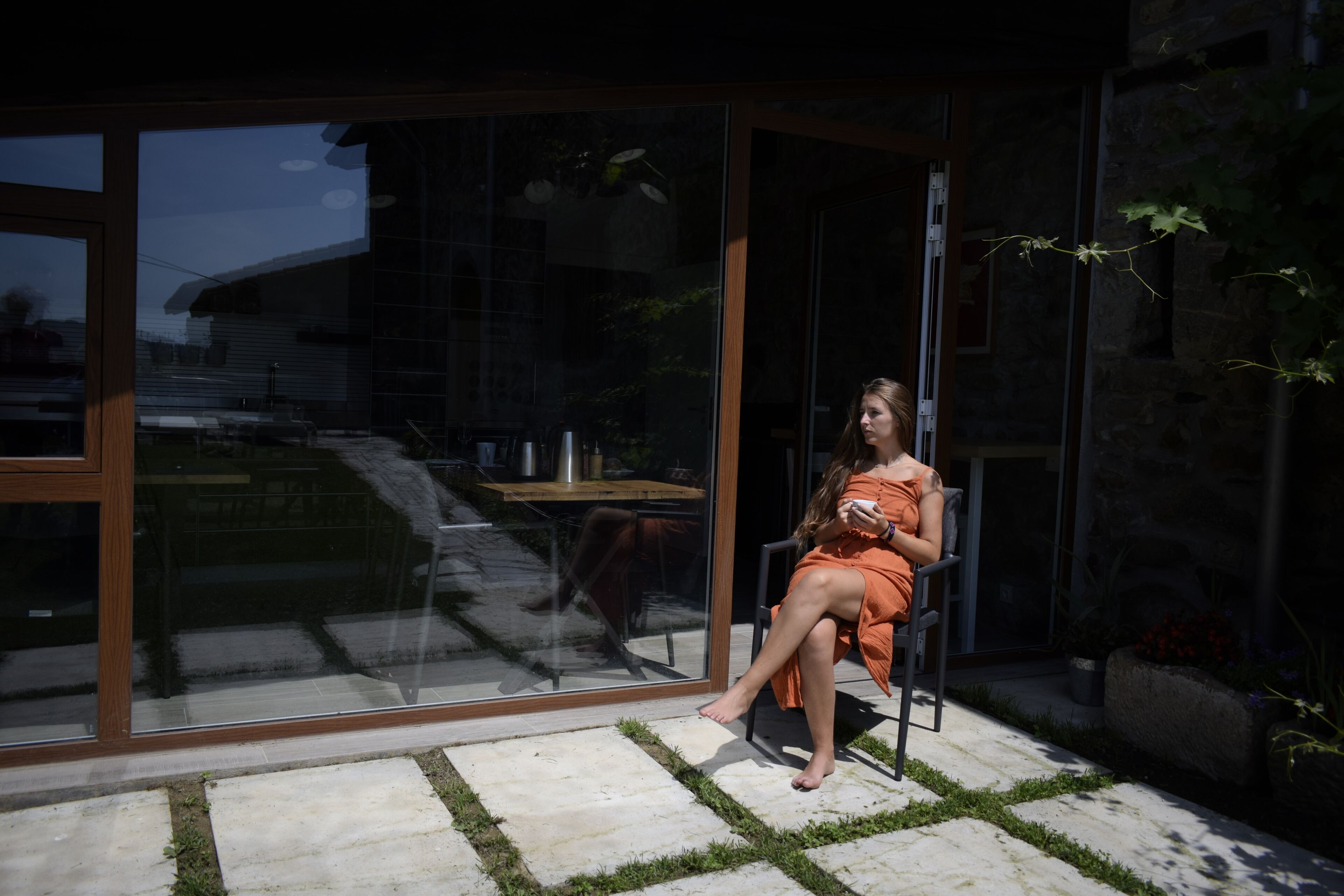 Una mujer sentada en una silla en un espacio exterior moderno con un ventanal de vidrio que da a un patio.