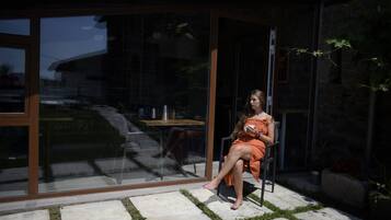 Una mujer sentada en una silla en un espacio exterior moderno con un ventanal de vidrio que da a un patio.