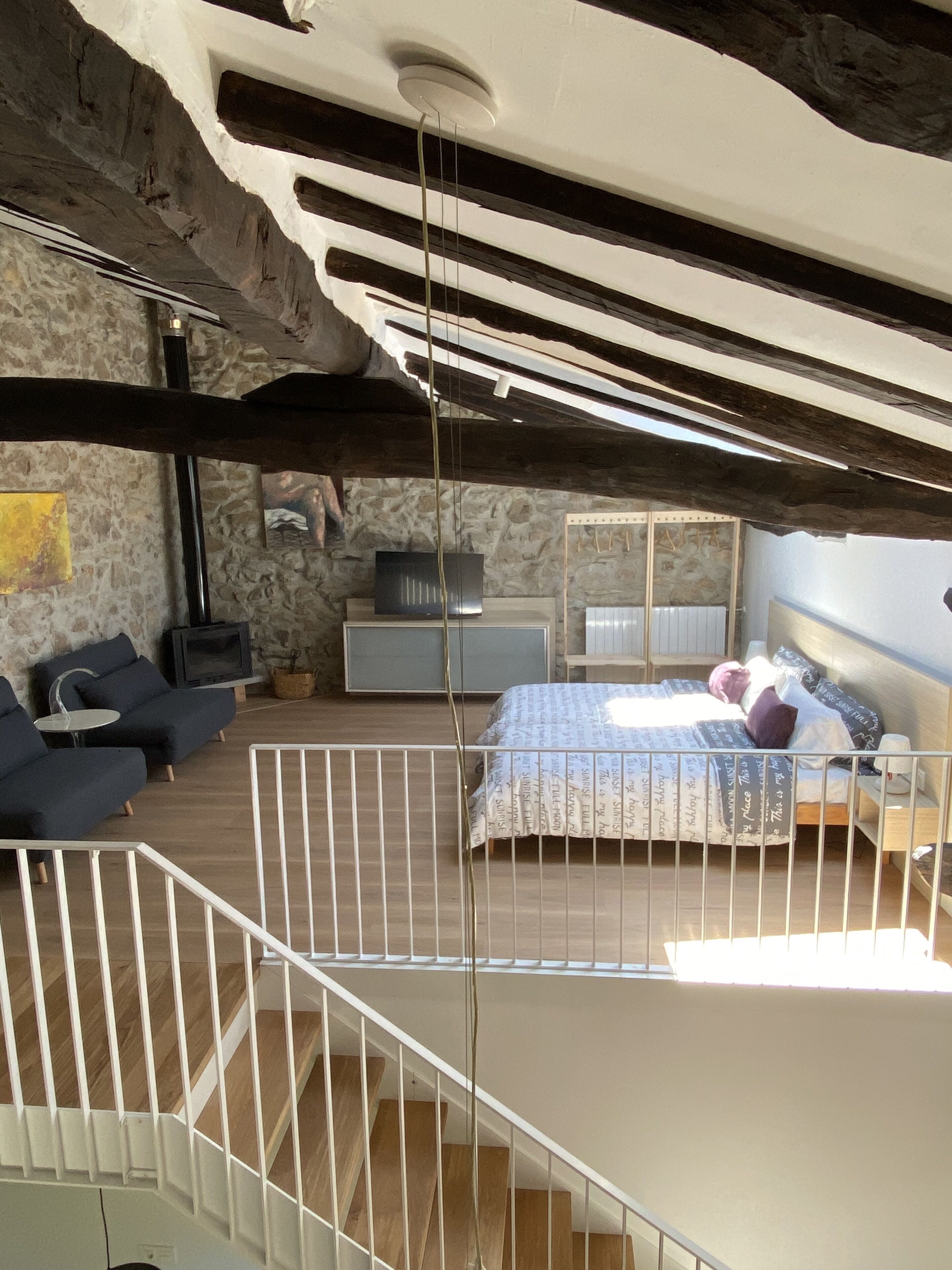 A bedroom with a bed, a sofa, a TV, and a stone wall.