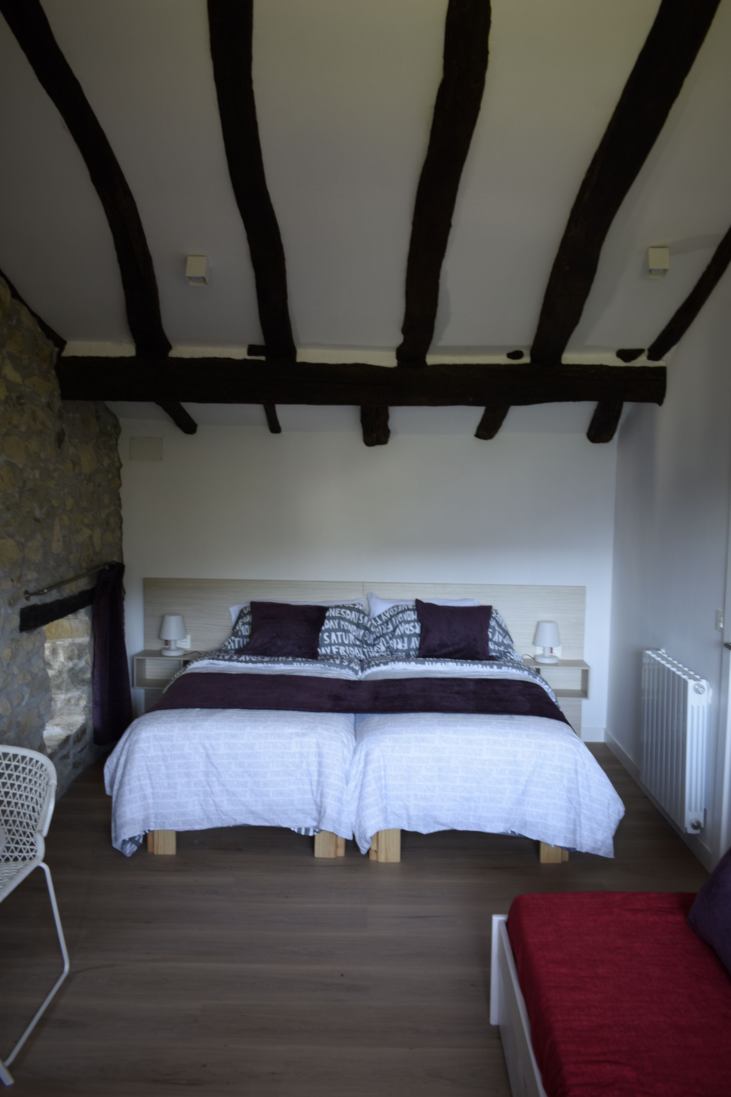 Un dormitorio con una cama grande, dos mesitas de noche, una silla y una pared de piedra.