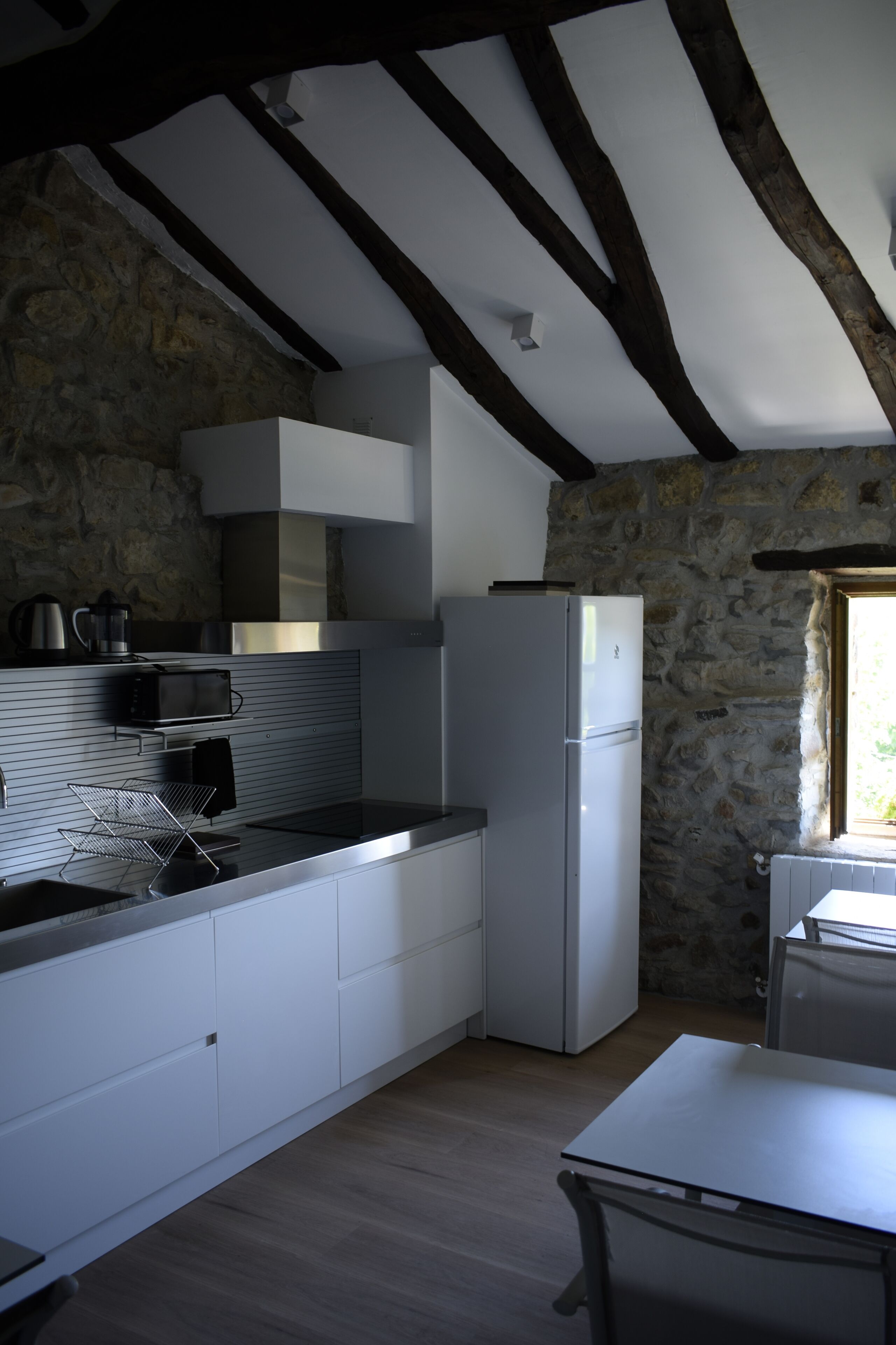 A kitchen with stone walls, wooden beams, a white refrigerator, a microwave, and a sink.