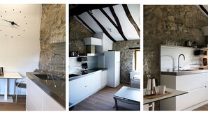 A modern kitchen with a stone wall, wooden beams, and a minimalist design. - Casa Rural Martiamuno Landetxea (Zumarraga)