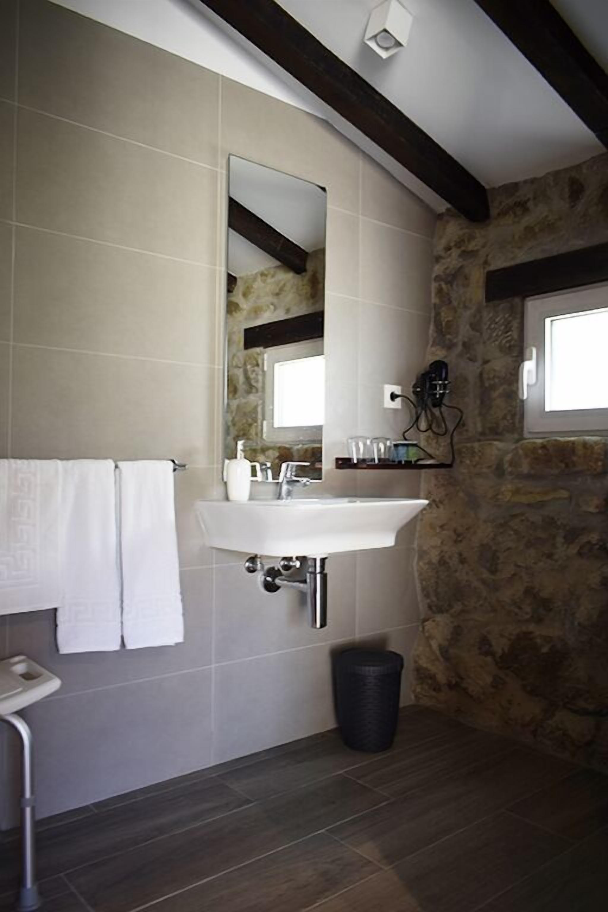 Un baño con un lavamanos blanco, un espejo, un perchero para toallas y una pared de piedra.