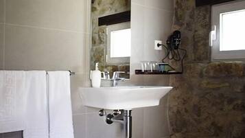 Un baño con un lavamanos blanco, un espejo, un perchero para toallas y una pared de piedra.