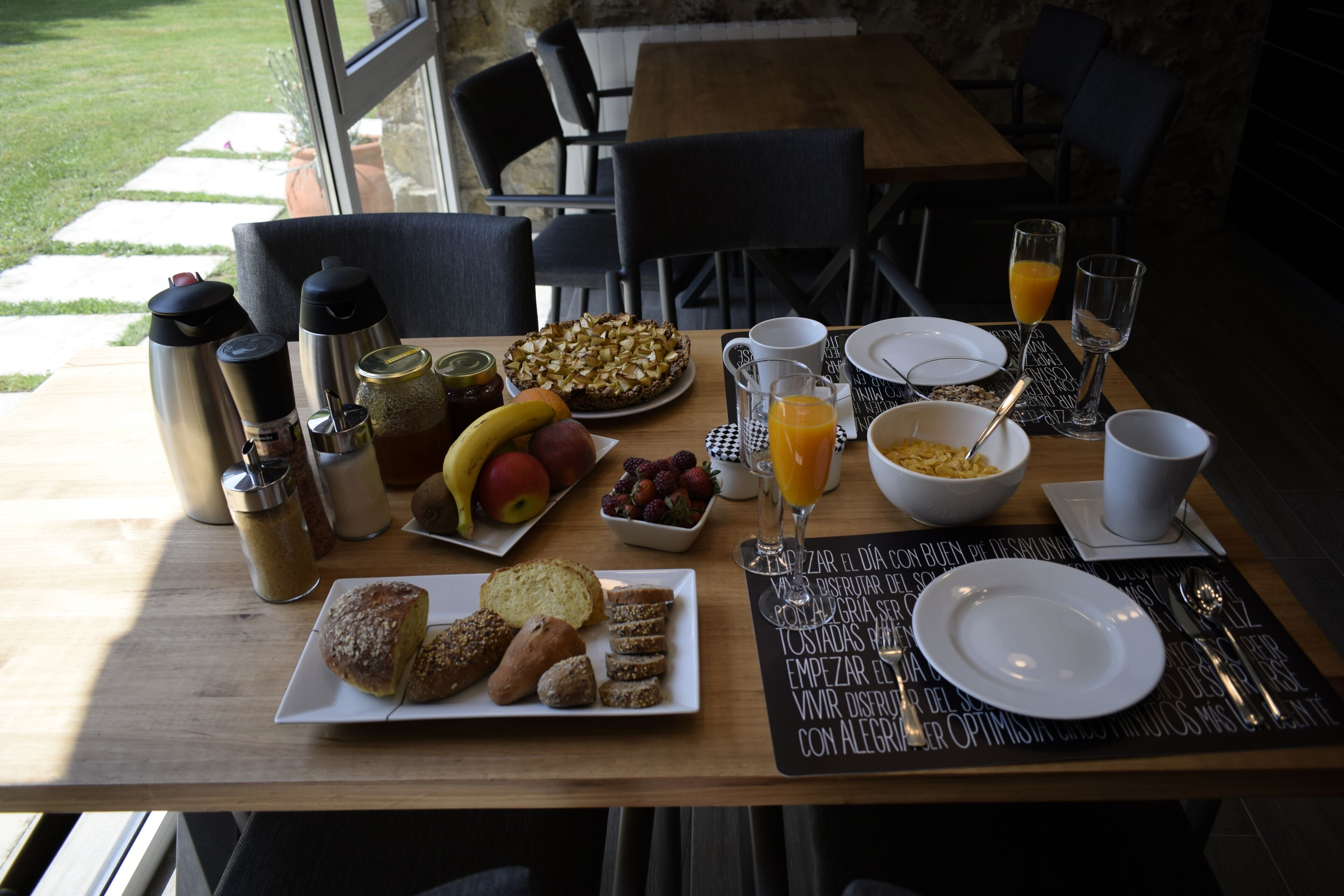 A breakfast table with various food items, including fruits, bread, and a pie, along with coffee and juice.