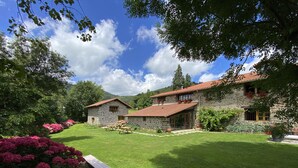 A stone house with a red-tiled roof, surrounded by a well-maintained lawn and flowering plants. - Casa Rural Martiamuno Landetxea (Zumarraga)