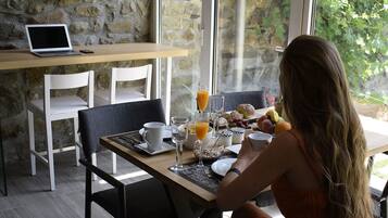 Une table mise pour le petit-déjeuner, avec un ordinateur portable, une tasse, un verre de jus d’orange et une assiette de nourriture.