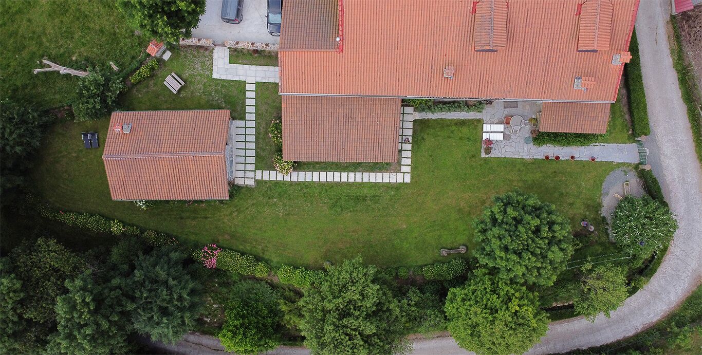 An aerial view of a residential area with multiple houses, a paved driveway, and surrounding greenery.