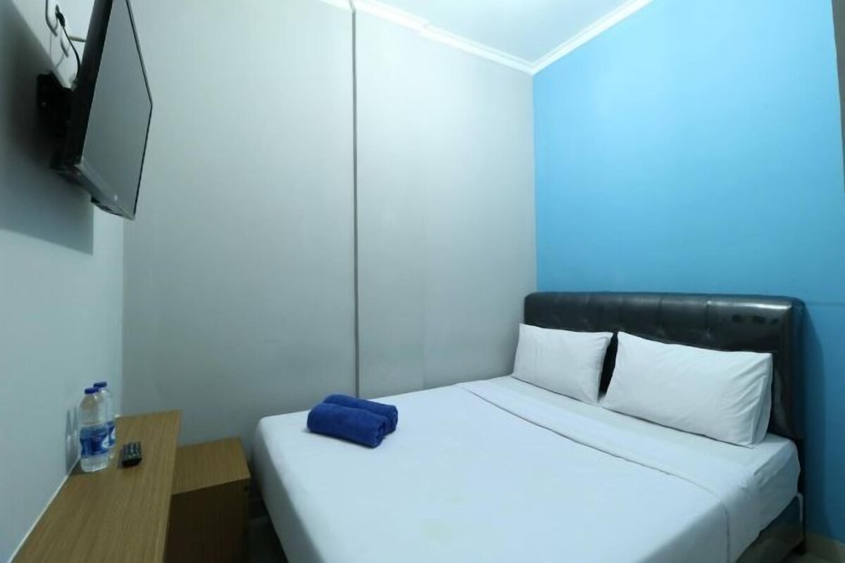 A hotel room with a bed, a nightstand, a TV mounted on the wall, and a water bottle on the nightstand.
