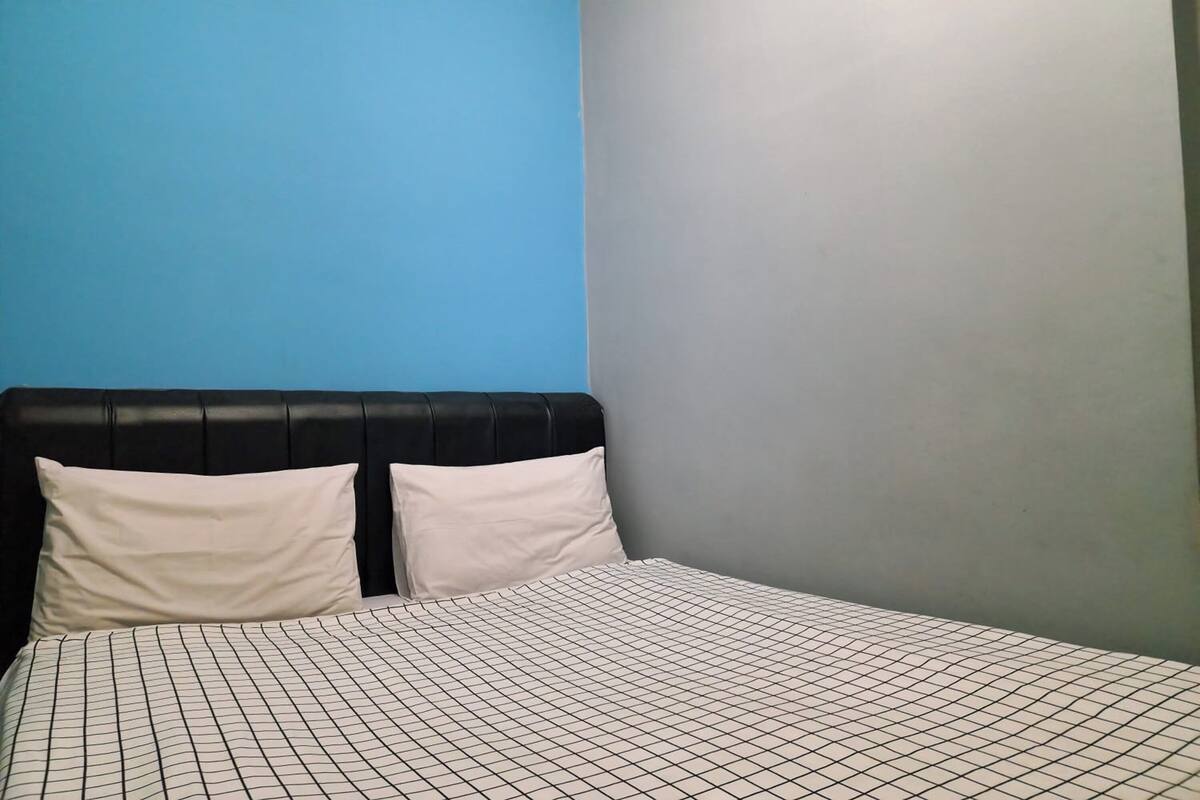Uma cama com cabeceira preta e almofadas brancas, diante de uma parede azul e cinza.