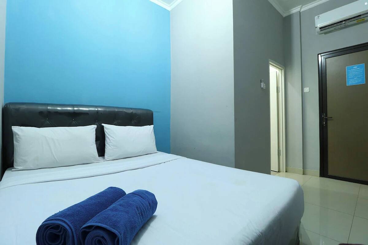 Quarto de hotel com cama, paredes azuis, porta e aparelho de ar condicionado.