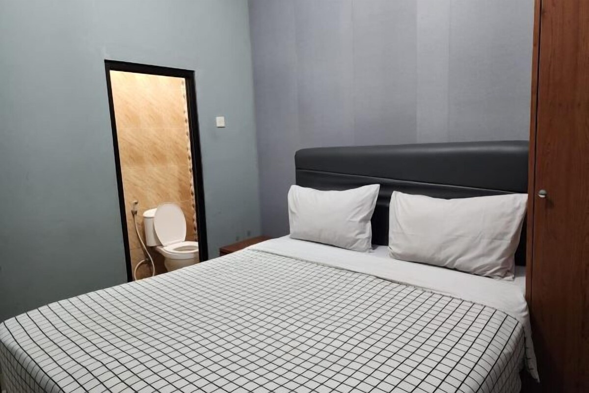 A bedroom with a bed, two pillows, a wooden door, and a toilet visible through an open door.
