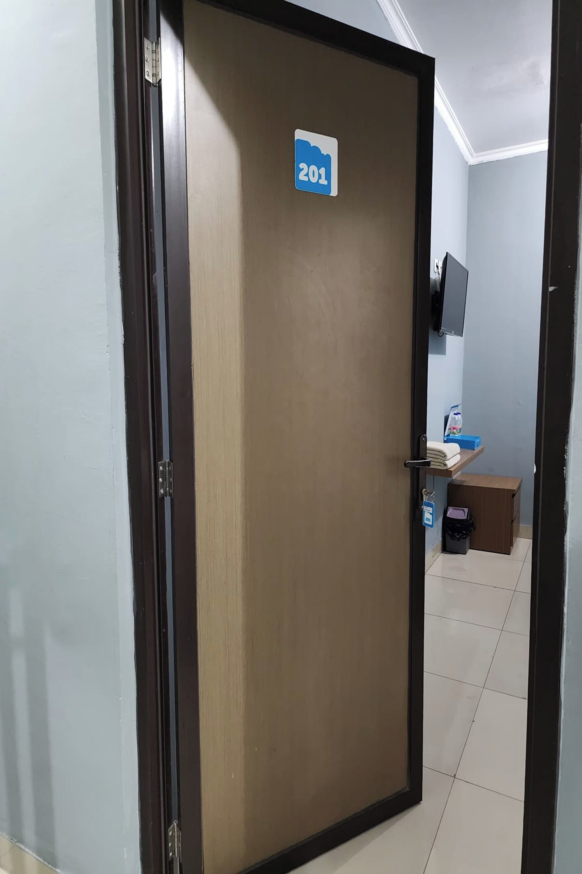 A hotel room door with a number sign, a small desk with a computer, and a trash bin.