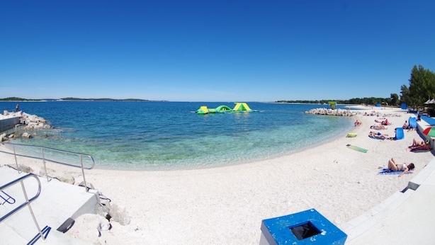 Ein Strand mit klarem Wasser, sandigem Ufer und einigen aufblasbaren Spielzeugen.