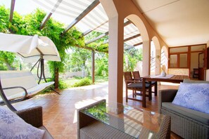 A covered outdoor seating area with a table and chairs, a wicker sofa, and a glass-top table. - Spacious holiday apartment with big covered terrace in village Valbandon (Valbandon, Fažana)