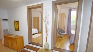 Ein modernes Hotelzimmer mit einem Holztisch, einem großen Spiegel, einer Vase mit Zweigen und einem Bett mit weißer Bettdecke.