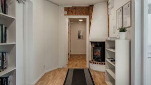 Un estrecho pasillo con suelo de madera, paredes blancas y una alfombra negra. Se observan estanterías a ambos lados, una chimenea y certificados enmarcados en la pared.