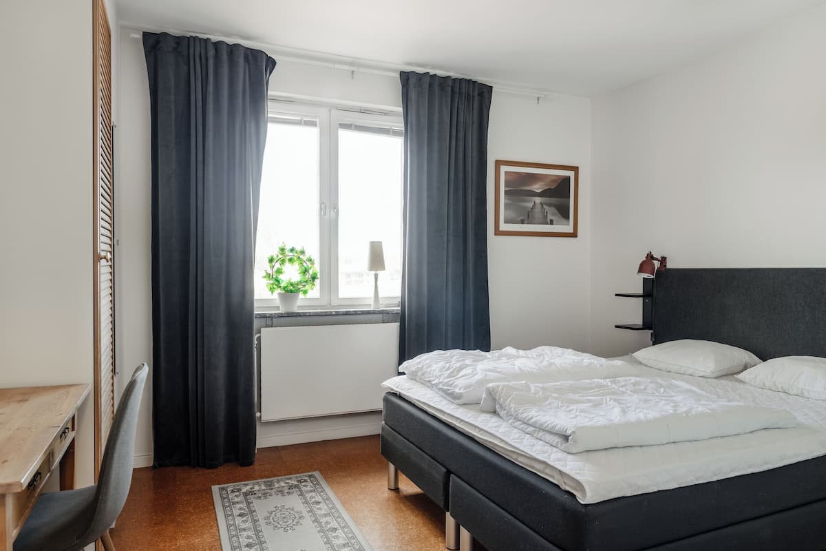 A bedroom with a bed, a desk, and a window with curtains.