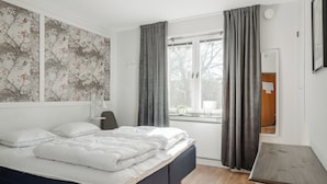 Un dormitorio con cama, un escritorio, una ventana con cortinas y una pared con estampado floral.