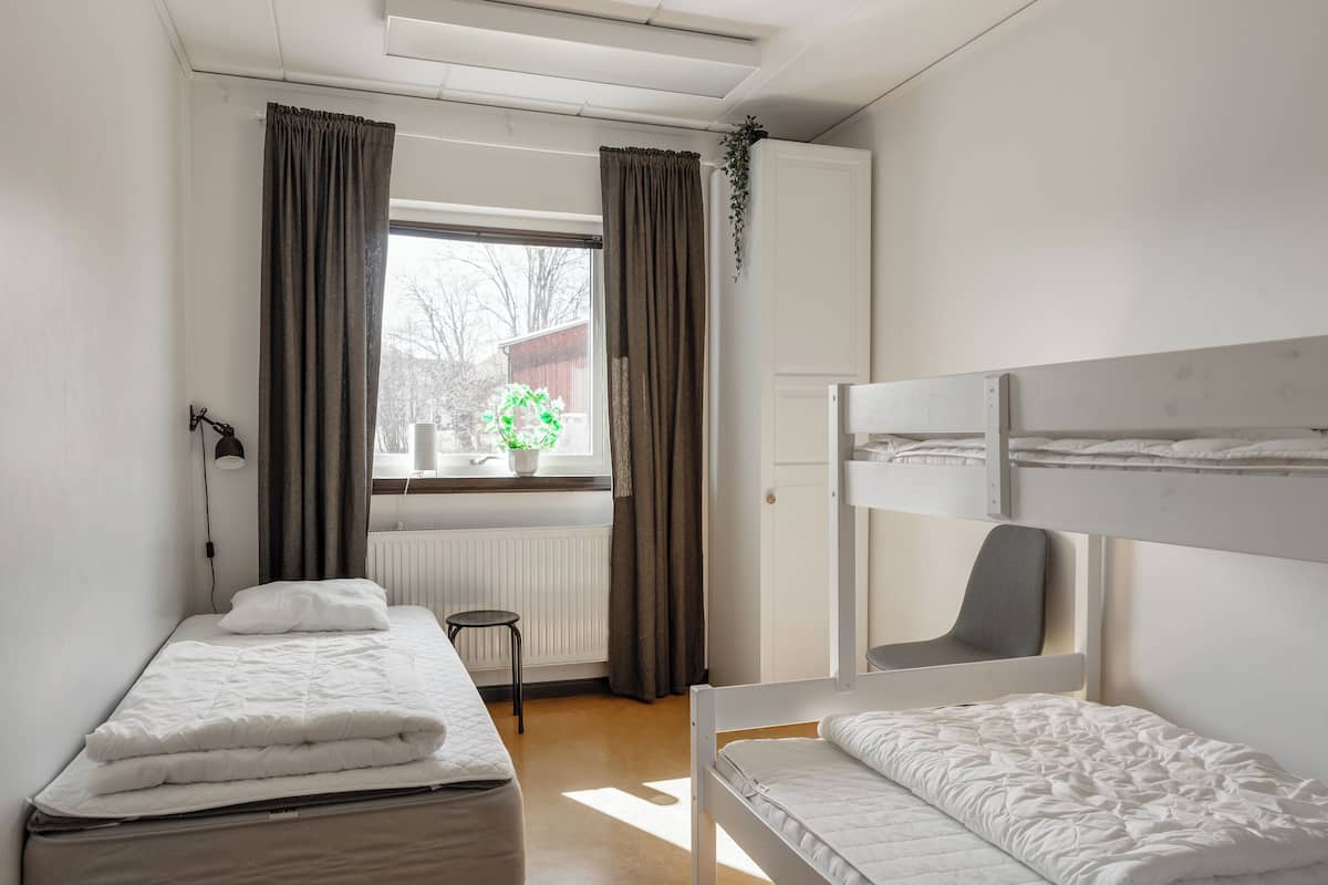 A room with two beds, a window with curtains, a radiator, and a small stool.