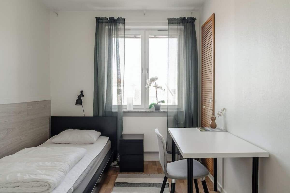 A bedroom with a bed, a desk, and a window with curtains.