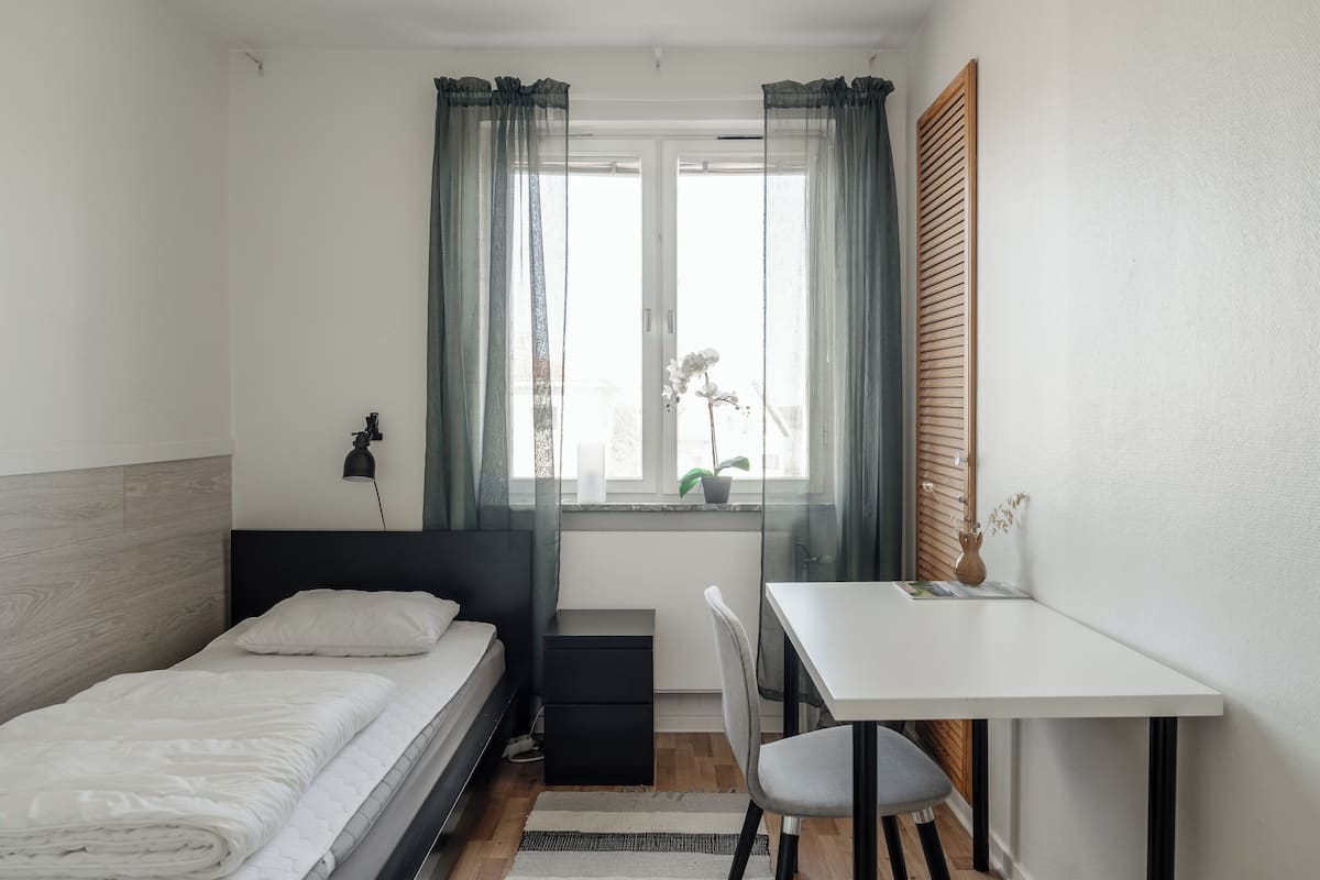A small, neatly arranged bedroom with a single bed, a desk, and a chair.