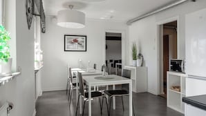 Una cocina moderna con muebles blancos, un comedor con mesa y sillas blancas, y un vano visible que da a otra habitación.